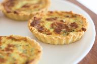 Kleine Quiches mit goldbraunem Teig und überbackener Füllung auf einem weißen Teller