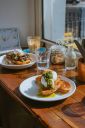 Mit Eiern und Grün garnierte Brunch-Teller auf einem Holztisch neben einem Fenster