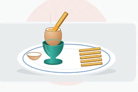 Unpeeled soft-boiled egg in a ceramic egg cup with its cap sliced off to show a runny yolk, and several buttered toast soldiers lined up beside it