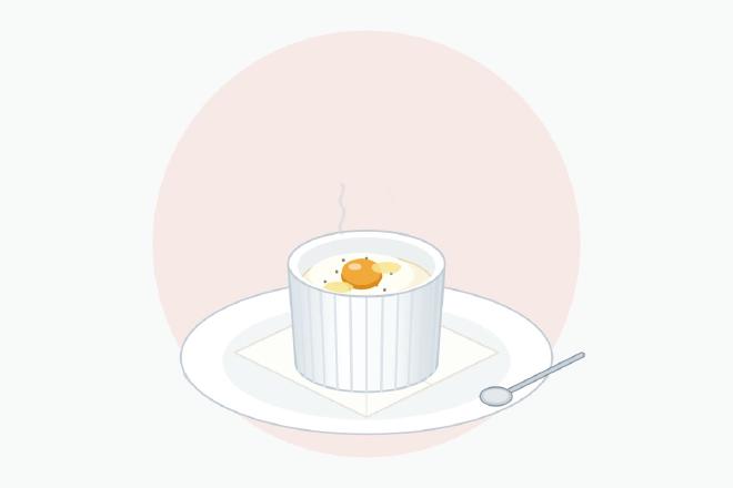 Egg en cocotte with cream in a small white ramekin on a folded napkin, white fully set and a glossy yolk ready to be broken with a spoon