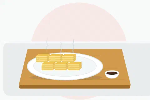 Sliced tamagoyaki showing its thin golden layers of egg, served on a plate with a small dish of soy sauce on the side