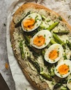Tostada con aguacate, mitades de huevos cocidos, hierbas y semillas sobre un plato claro