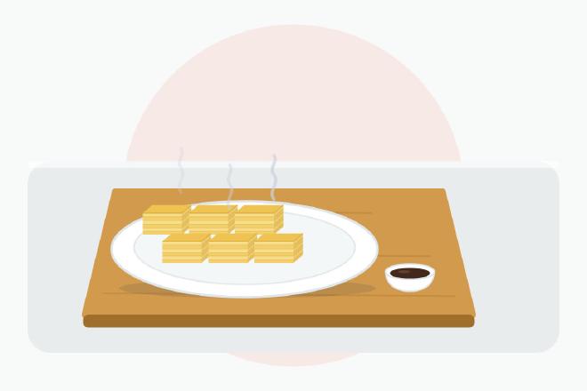 Tamagoyaki cortado en rodajas que muestra sus finas capas doradas de huevo, servido en un plato con un pequeño cuenco de salsa de soja